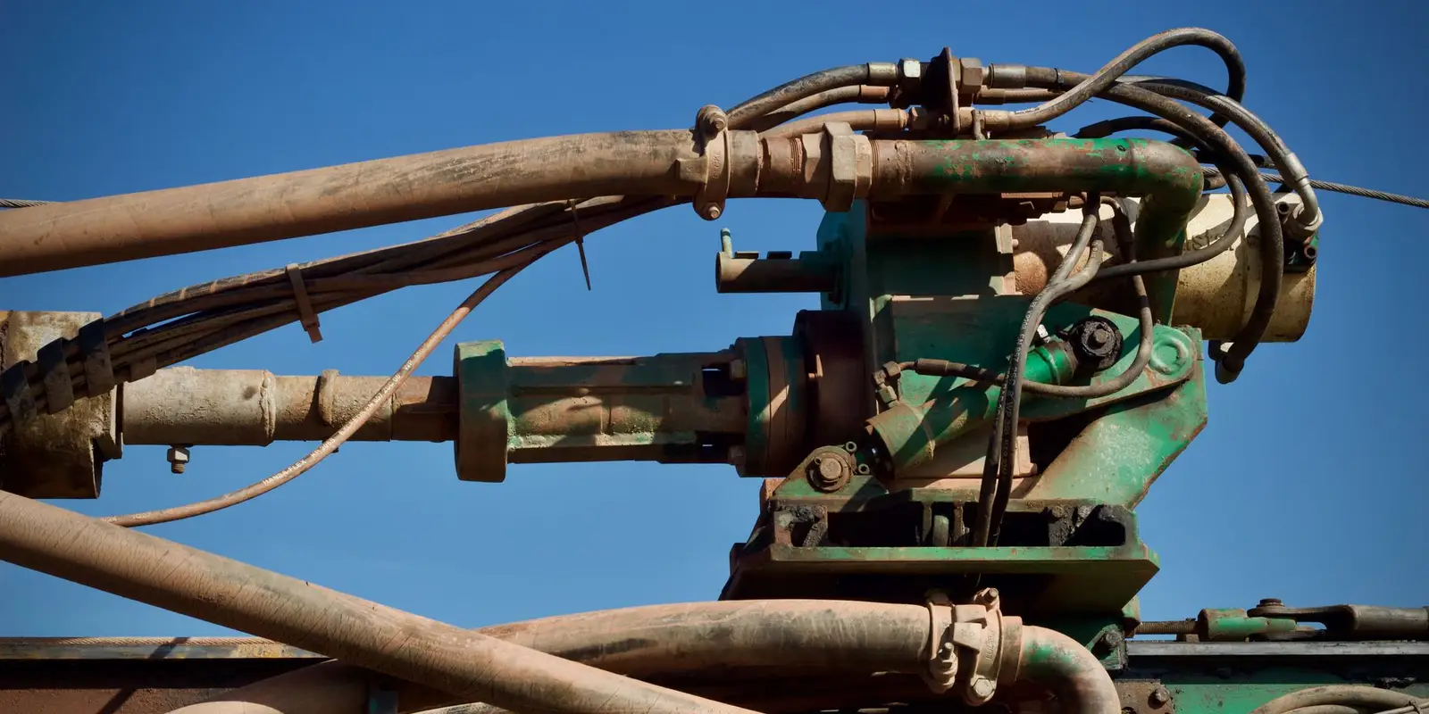 Hydraulic hoses, fittings and cylinders on a drilling rig against a clear blue sky