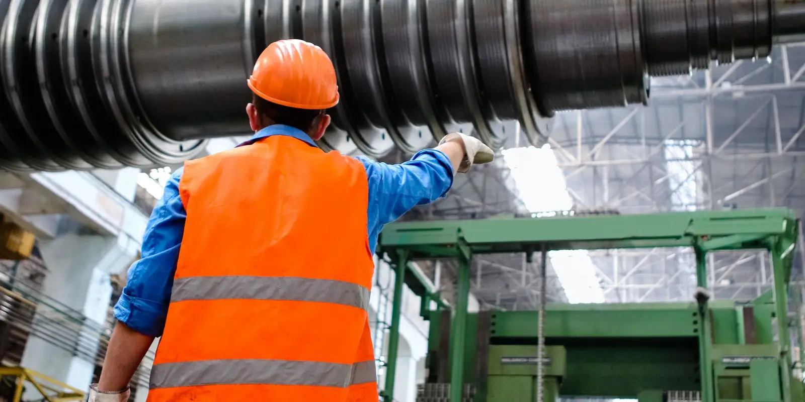 Engineer in high visibility gear inspecting a large machine rotor in a workshop