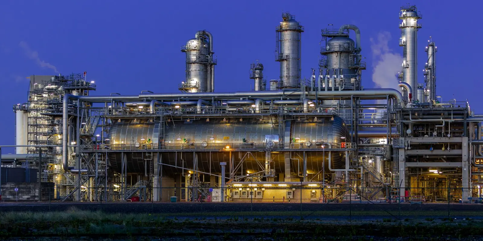 Process plant vessels and pipework lit up against a deep blue dusk sky