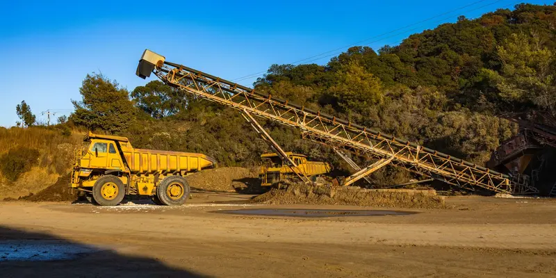 Haul trucks and a stacker conveyor at a mining site in evening light